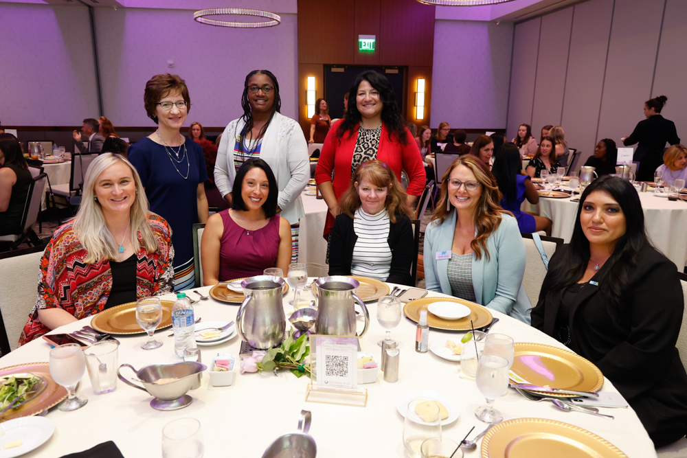 8 women smiling for picture around circle dinner table