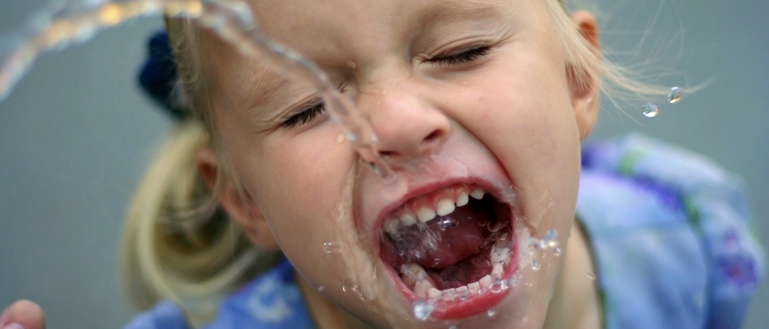 A little girl drinking from a water fountain.